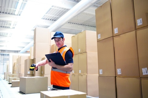 Arbeiter im Versandhandel scannt Pakete am Fliessband zur Lieferung ein // Mail-order workers scan packages on conveyor belt for delivery